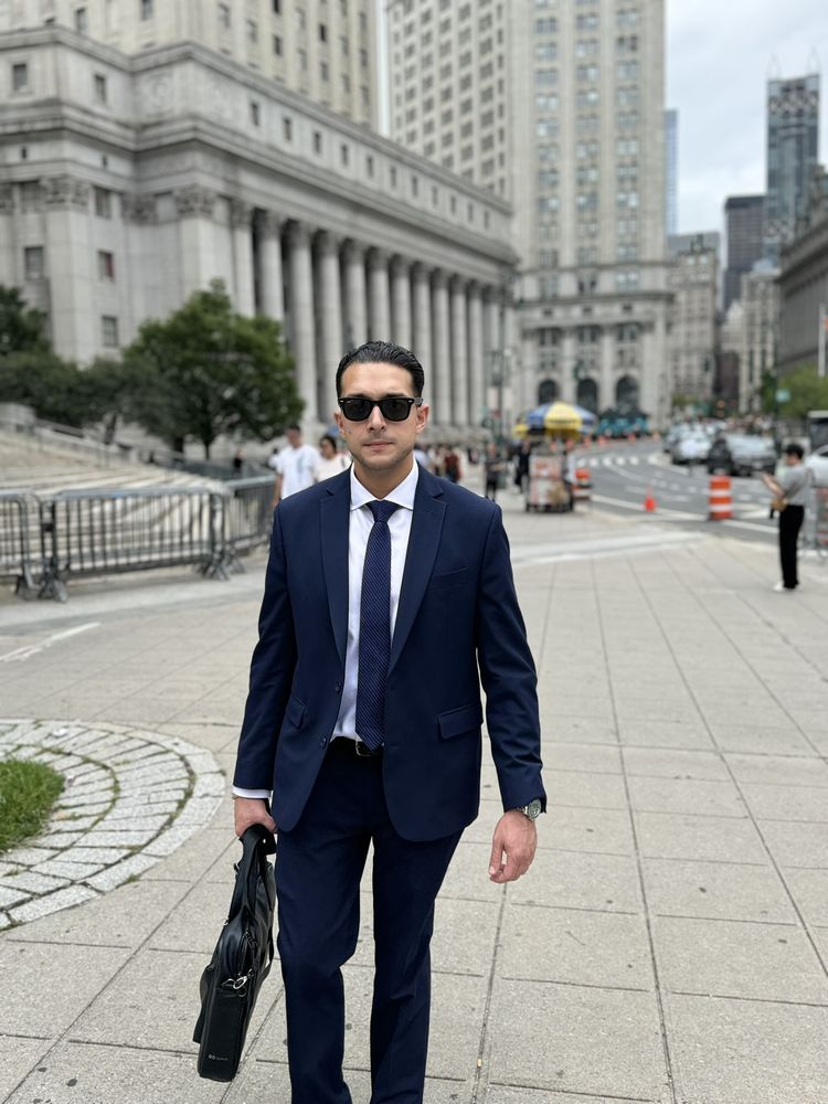 Migir Ilganayev walking away from a Lower Manhattan courthouse in a navy suit, carrying a briefcase.
